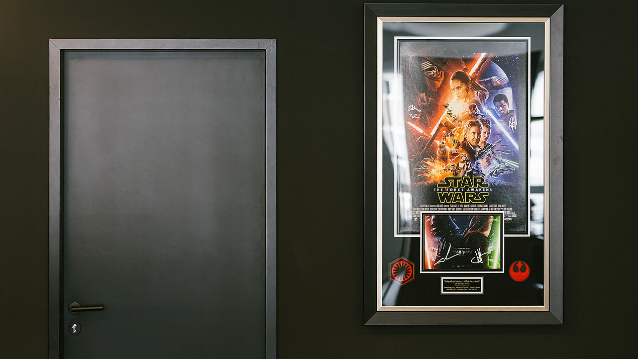 Gerahmtes Filmplakat von „Star Wars: The Force Awakens“ hängt an einer dunklen Wand neben einer geschlossenen Tür, präsentiert als dekoratives Wandelement.